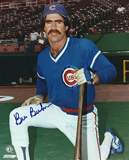 Bill Buckner with next-level eyebrows and mustache, dressed in a Chicago Cubs home uniform. He is kneeling on his left knee and resting his left hand on a baseball bat.