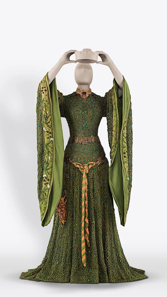 A mannequin posed in a long green medieval style dress with long hanging sleeves and a gold belt