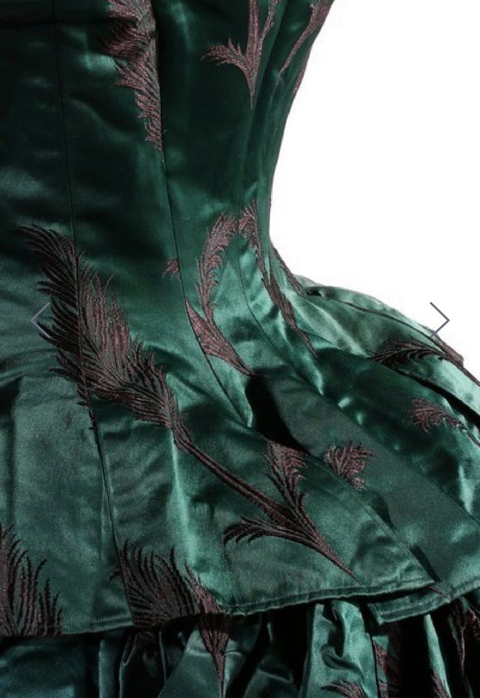 A detail of the back of the bottle green satin dress that focuses on the bottom of the bodice as it sits over the skirt