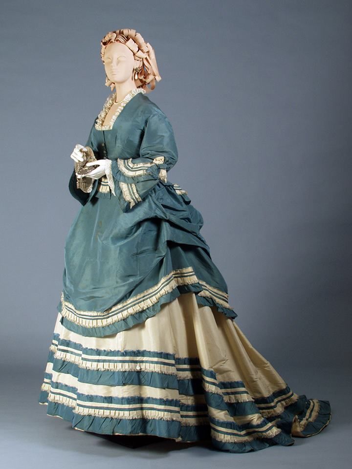 A blue and cream bustle style dress. The blue long lined polonaise bodice is trimmed with cream and the cream skirt is trimmed with blue 