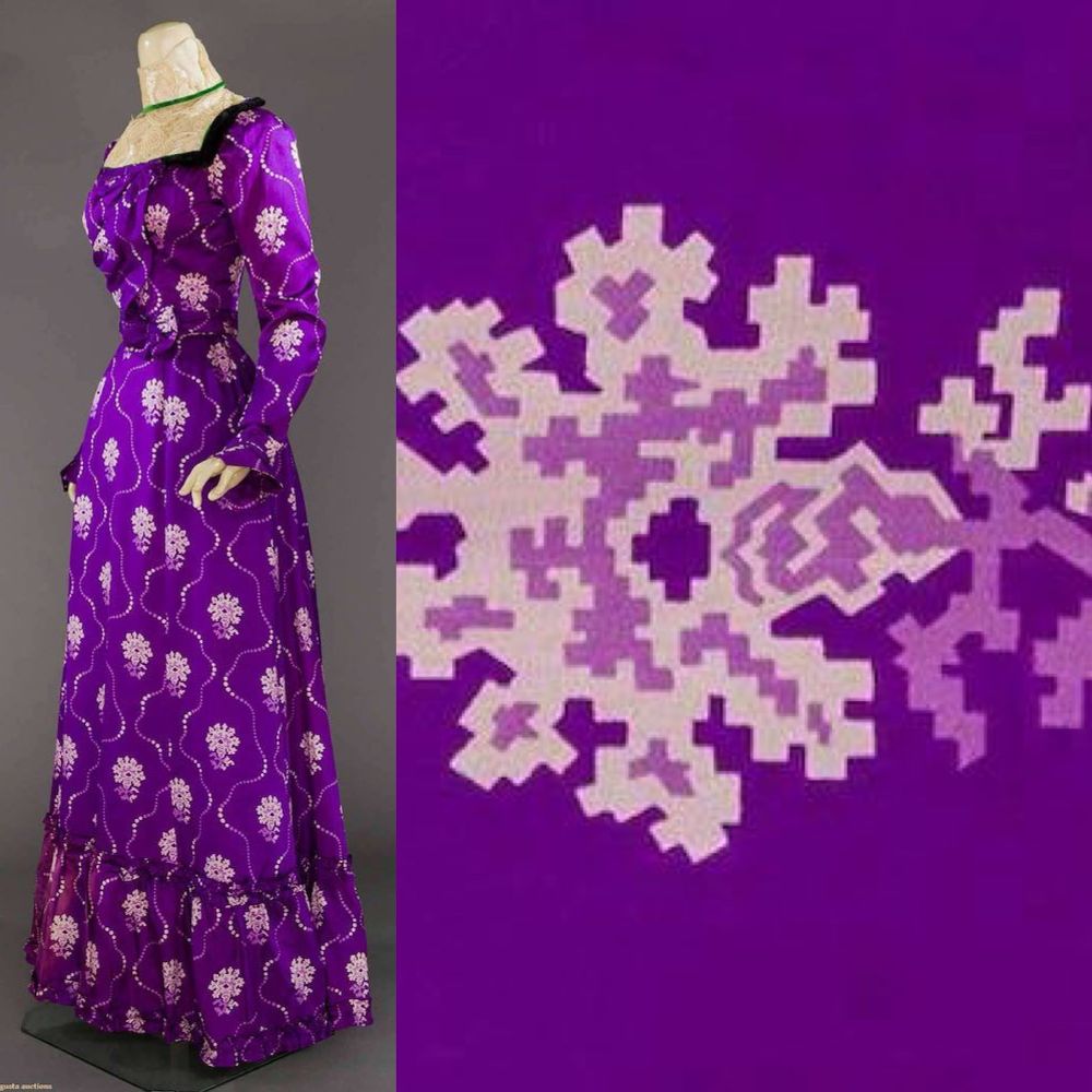 A photograph of a mannequin wearing a bright purple long silk gown with lace insert at the neck. It has a pixelated pattern of stylised flowers in pale purple a detail of which is shown