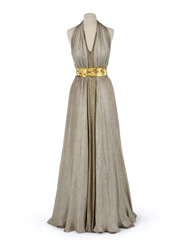 Front full length view of a sleeveless halter neck silver gown with a V neck and open robe style. It is cinched at the waist with a gold belt