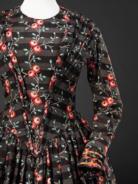 Bodice detail of a long sleeved floor length dress with dark horizontal stripes overprinted with leafy tendrils and red flowers