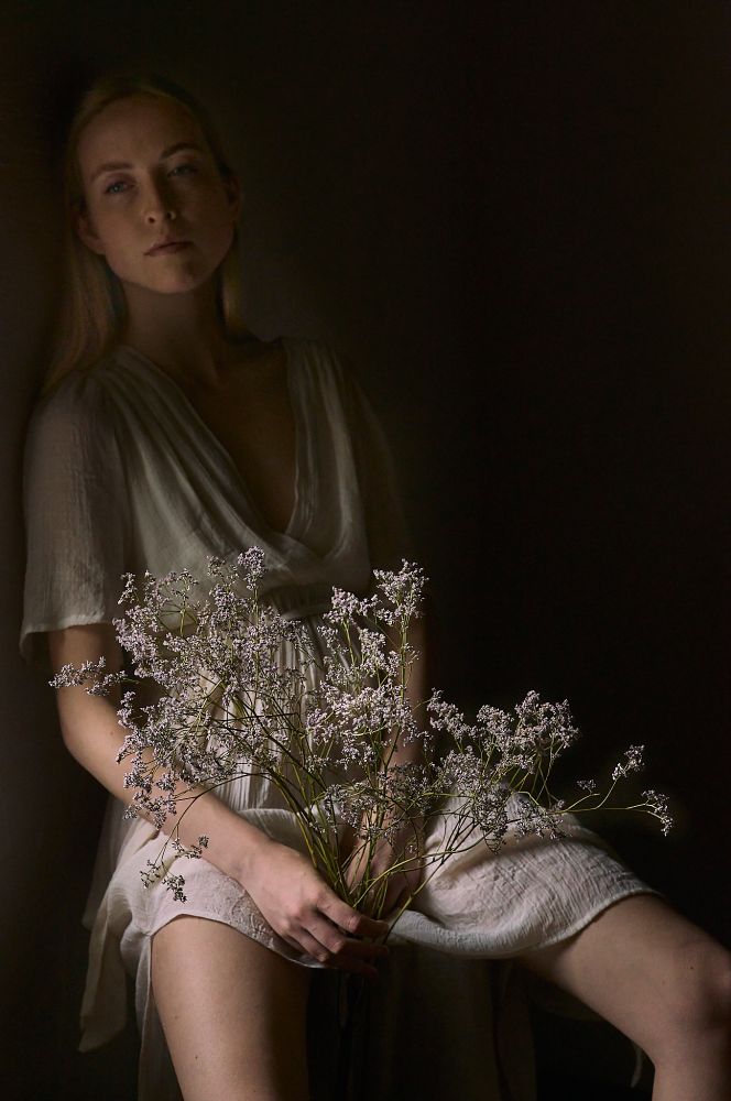 a Portrait of a young blonde woman wearing a wheat coloured dress and holding branches of small flowers