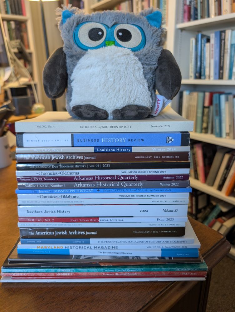 tall stack of print journals of various titles (owl stuffed animal sitting on top)