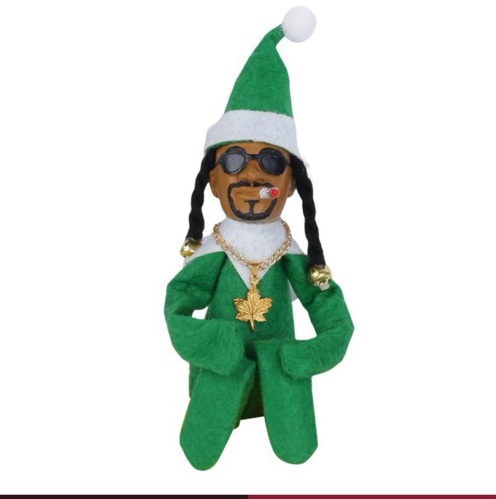 A photo of “snoop on a stoop” which is like the little “elf on the shelf” but with snoop. He’s wearing a gold chain with w marijuana leaf and is smoking a fattie.