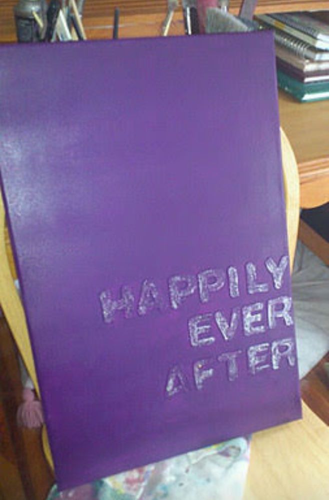 A canvas painted purple with a raised silver glitter message Happily Ever After 