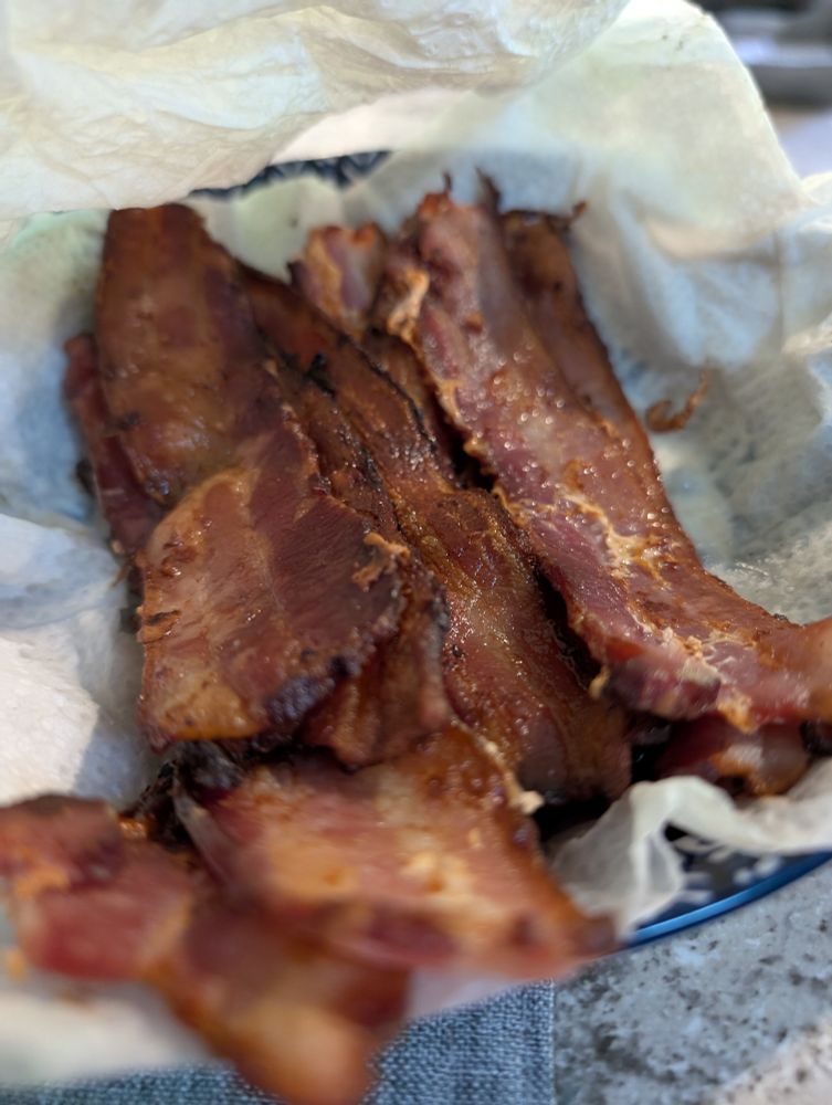 Thick bacon cooked on a charcoal BBQ grill sitting on a plate ready to eat