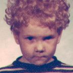 A kindergarten class photo of a five-year-old white boy with curly blonde hair, looking serious and no smile