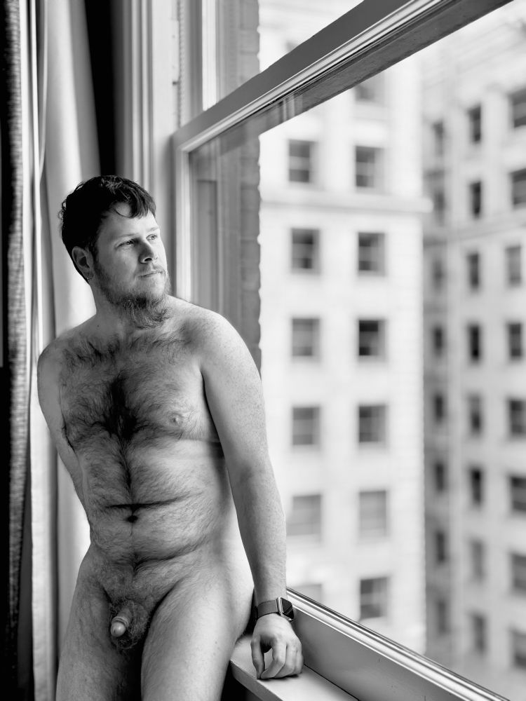 Naked hairy cub sitting on a windowsill looking out and enjoying their nudism indoors. 