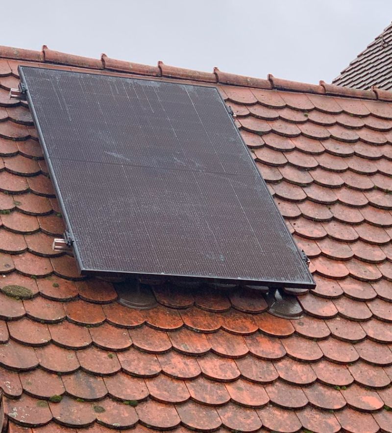 Man sieht ein Dach mit Biberschwanzziegeln und einem darauf montierten Solarmodul