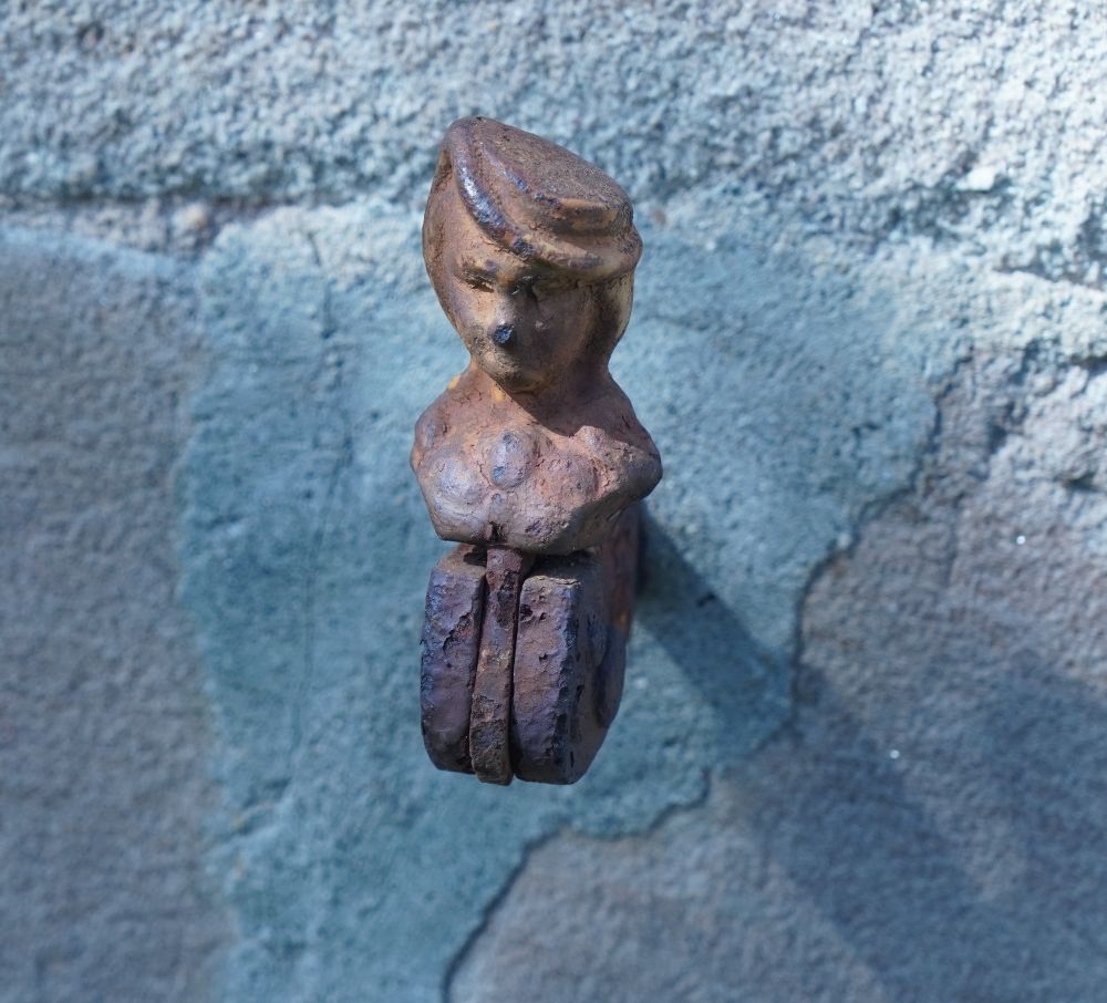 Man sieht an einer Wand einen Verriegler für Fensterläden. Ist eine Figur mit Mütze, die hier gezeigt ist