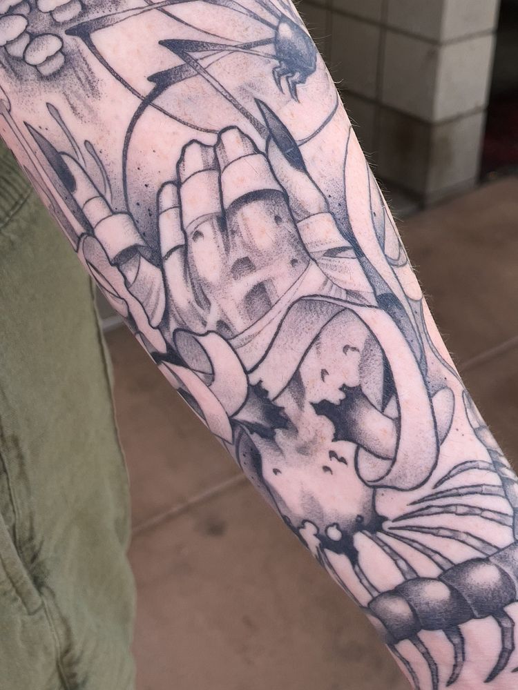 A tattoo depicting the face of an androgynous character with a snake moving through their eye sockets. Throughout the tattoo are mushrooms, plants, and other fantastic and floral imagery.