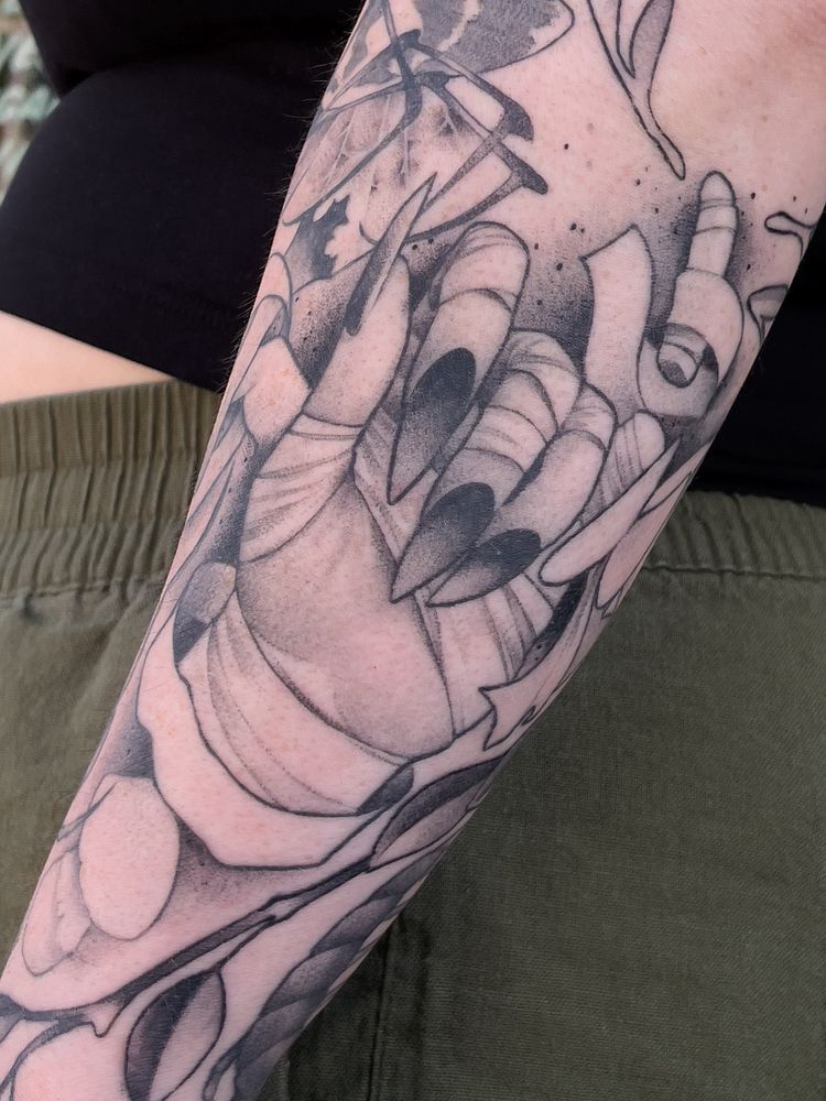 A tattoo depicting the face of an androgynous character with a snake moving through their eye sockets. Throughout the tattoo are mushrooms, plants, and other fantastic and floral imagery.