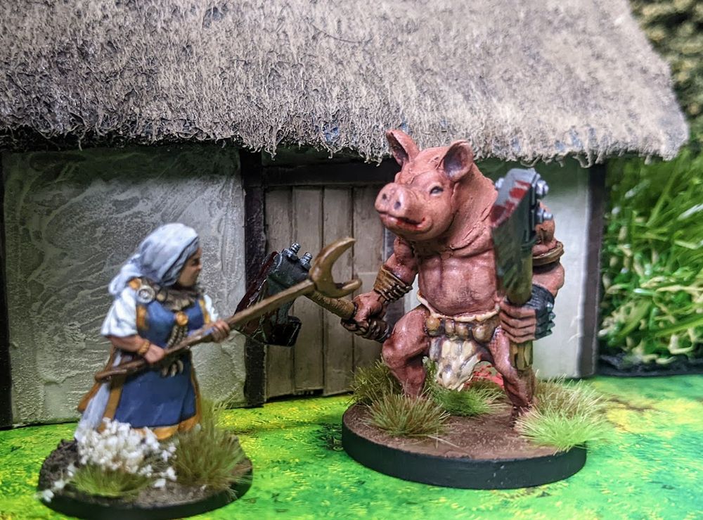 A scene with miniature figures: an axe-wielding, pig-headed monster menaces an old woman in front of a thatch-roofed cottage. She defends herself with a pitchfork. 