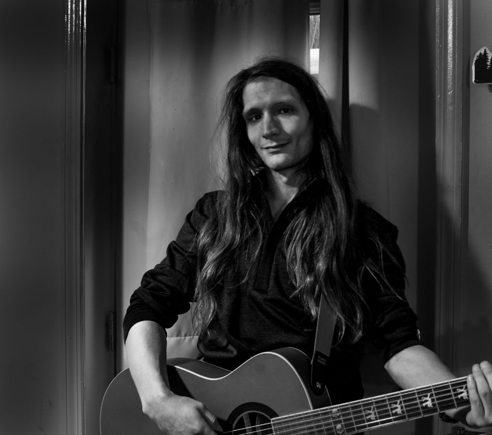 Black and White Photograph of a Man with Long, Wavy Hair Standing in the Center of a Doorway with a Curtain