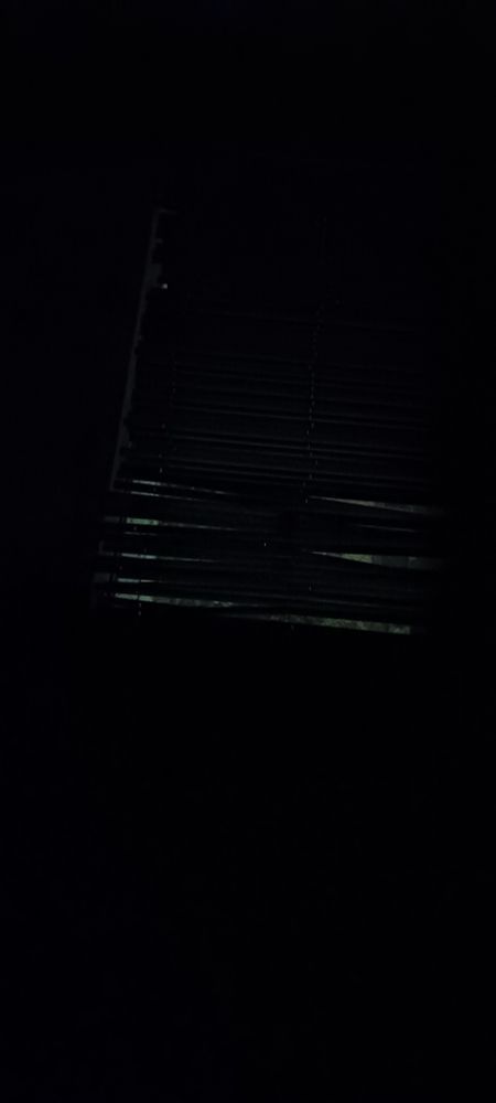 Uma foto escura de uma persiana quebrada, é possível ver a luz entrando pelas fendas