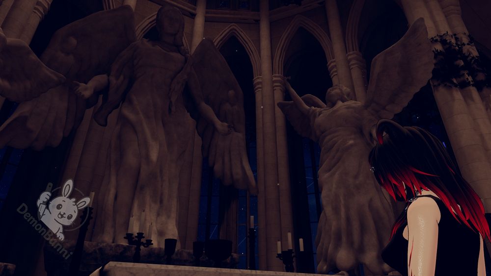 Photograph of a person with black and red hair standing in a church with large angel statues. The person is wearing a black top and has their back to the viewer. The angel statues are on either side of the person, and there are candles on the altar in front of them. The church has tall arches and columns, and there is a logo for "DemonBunni" in the bottom left corner.