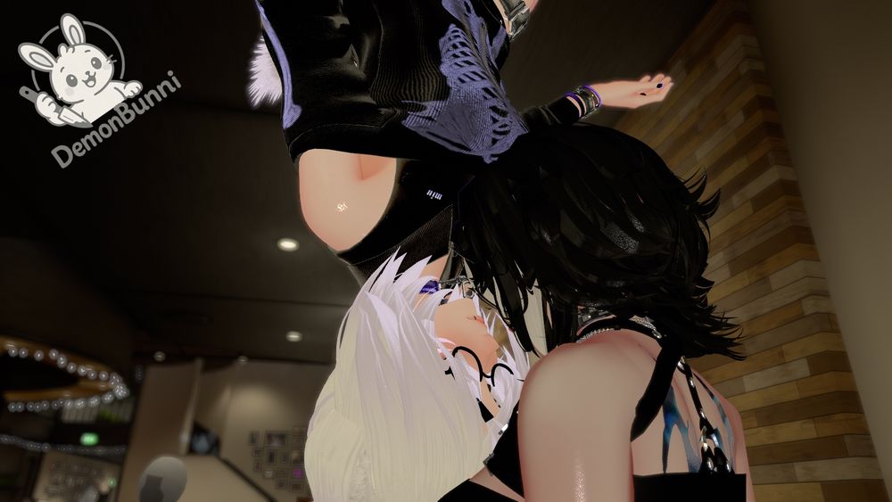 Photograph of two women in a virtual space, one upside down. The woman on the bottom has long black hair and is wearing a black top with silver straps. The woman upside down has long white hair and is wearing glasses, a black top, and black shorts with the word "miu" on them. In the background is a logo for "DemonBunni".