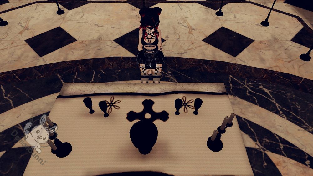 Photograph from a high angle of a person kneeling behind a table with occult symbols. The person has red hair, black bear ears, a black top with a pentagram, and a black skirt. The table has a cross in the center, with two sets of symbols on either side, and two candelabras on the edges. The floor is a checkered pattern of black and white marble. A logo for DemonBunni is in the bottom left corner.