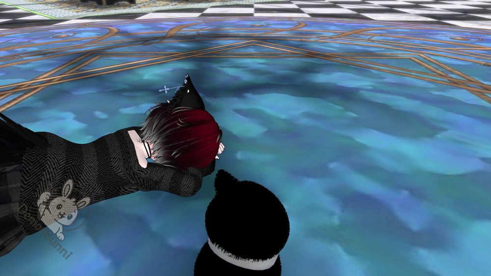 Photograph of a digital avatar with red and white hair, wearing glasses, a black outfit, and cat ears, lying on a blue floor with a gold design. A black cat plush is next to the avatar. The floor above is checkered black and white. A logo of a white bunny with the word "Bunni" is on the avatar's outfit.