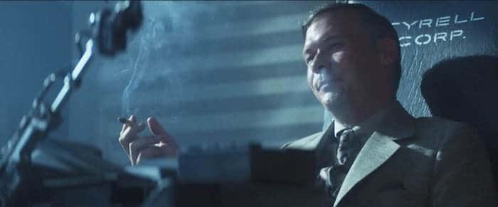 Man in a suit smoking, with 'Tyrell Corp' behind him. (Still from 'Blade Runner'). 