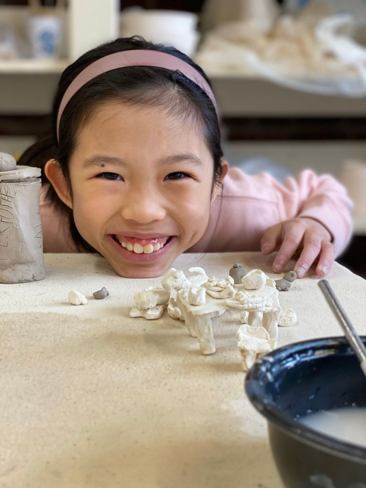 8 year old smiling next to tiny clay furniture and pets