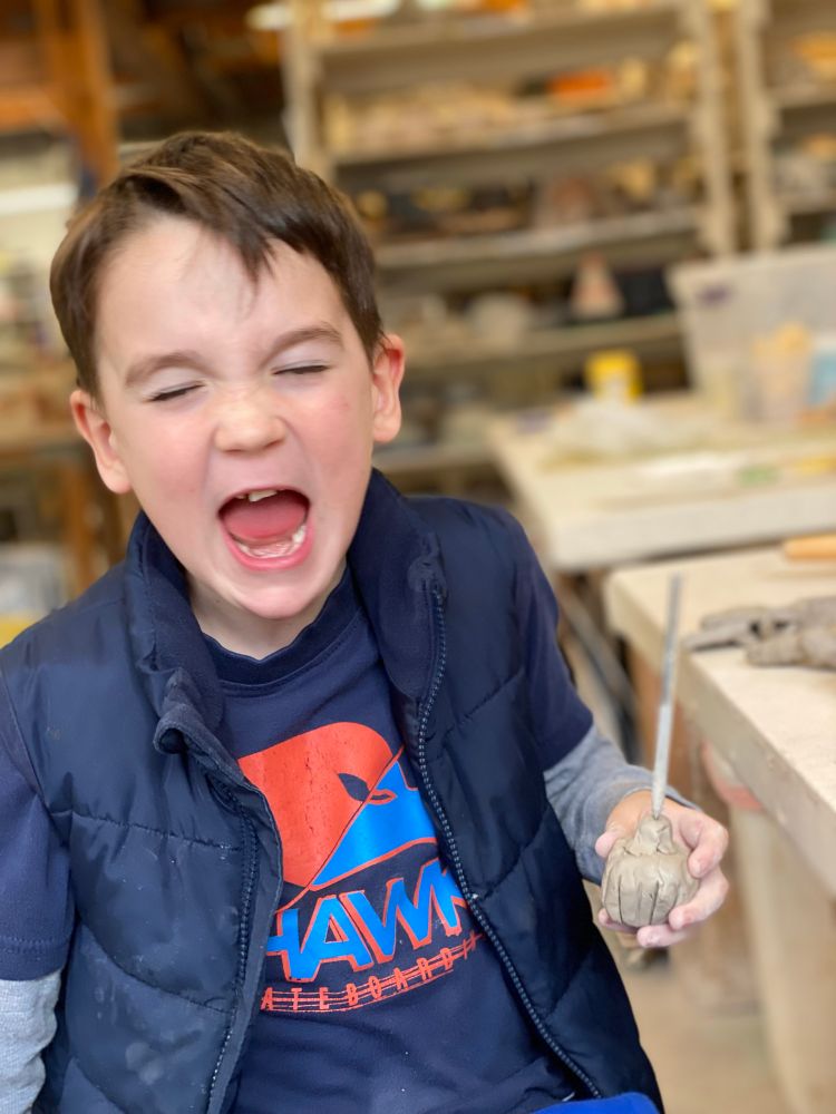 Child being silly with a clay pumpkin and tool.