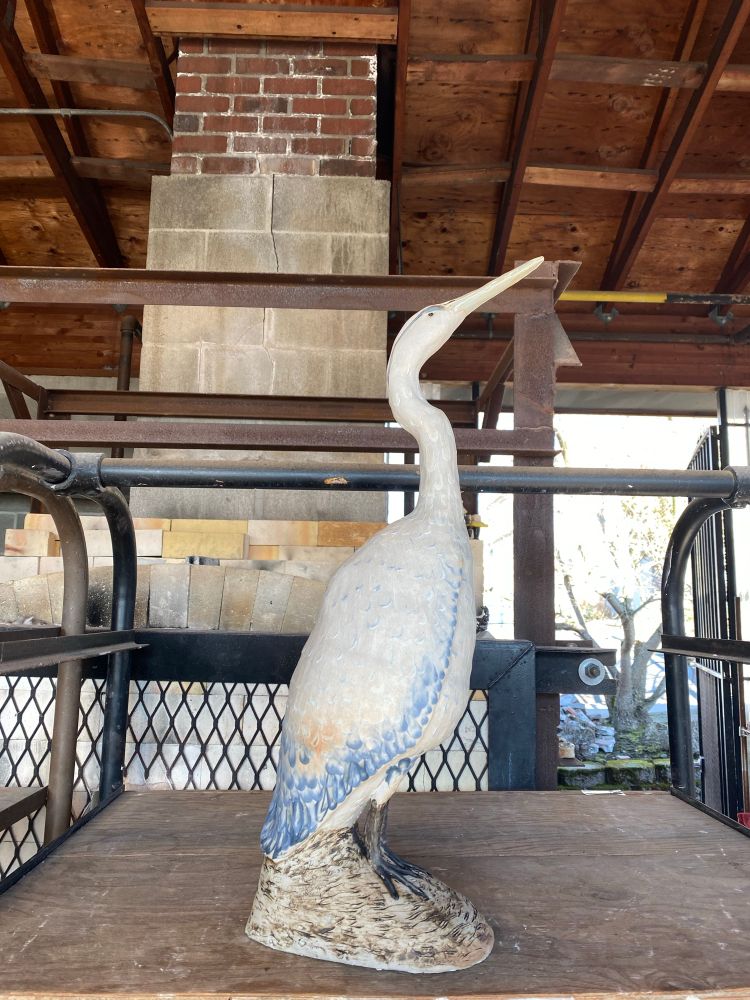 A ceramic sculpture of a heron with blue feathers, sitting atop a rock.