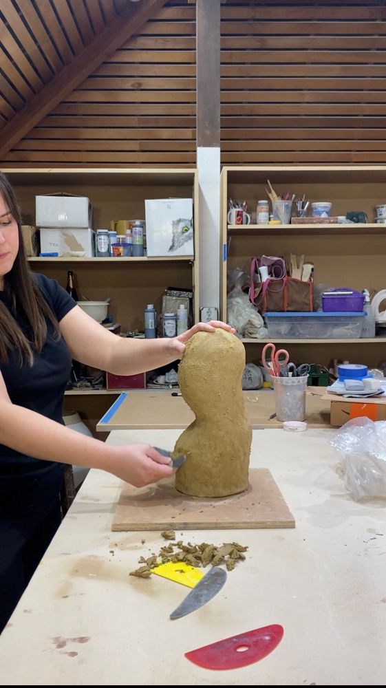 An artist uses a serrated rib tool to smooth an unfinished clay sculpture.