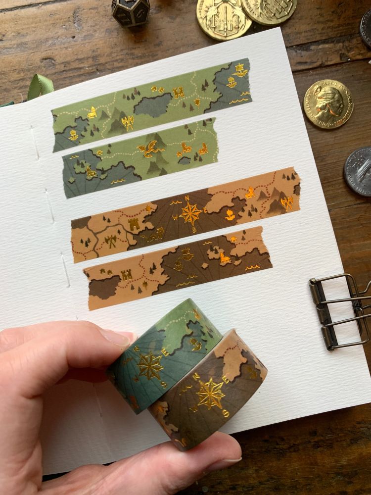Two rolls of washi tape, one green and one brown, with a gold foil fantasy map design 