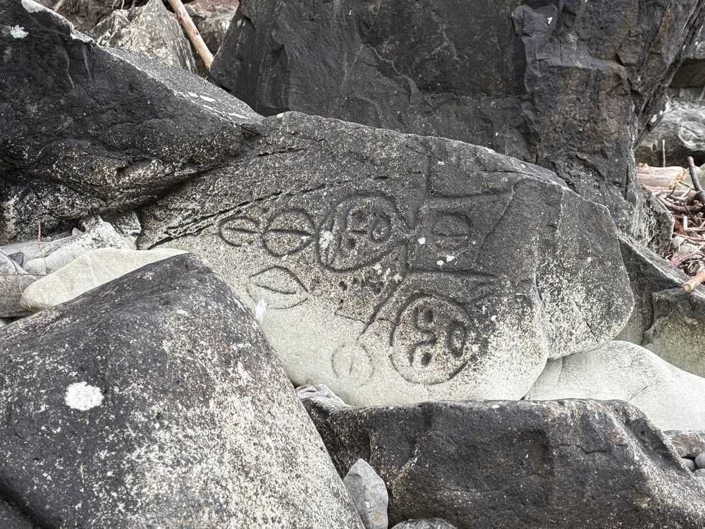 Carvings depicting figures on a rock on a gray Pacific Northwest beach