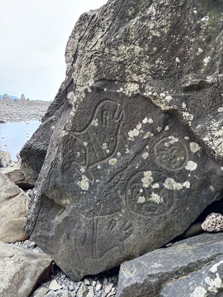 Carvings depicting orcas and faces on a rock on a gray Pacific Northwest beach