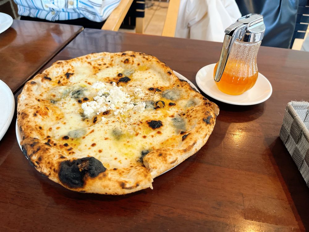 INAXライブミュージアムの中にあるレストランで食べたピザ、クアトロフォルマッジ
ブルーチーズとリコッタチーズしか分からないがクアトロというからには多分あと2種類のチーズがある
ピザの横にはオレンジがかった蜂蜜の入った瓶がある