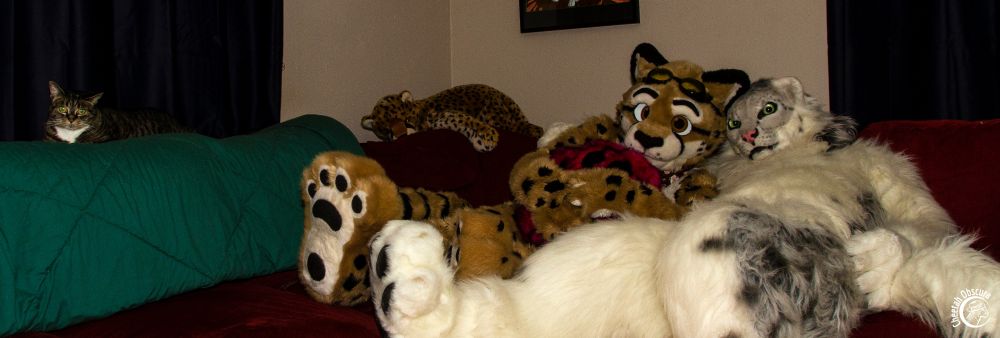 Photo of Obscura and Kieran cuddling on a sofa with a tabby cat loafed on the sofa back off to the side