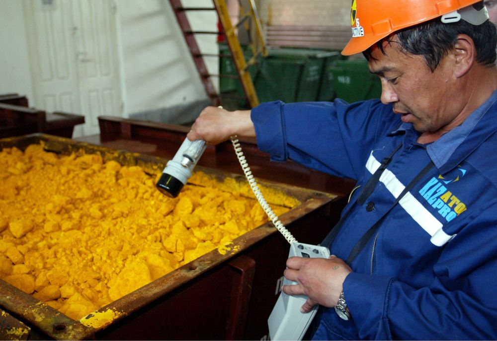 Man measuring yellow cake with a radiation detector. He has no gloves or respirator and the bin is open, large, and there are visible piles of yellow dust around