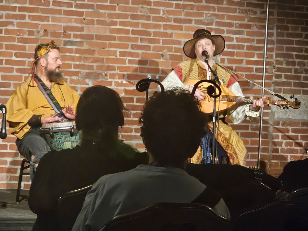 An audience member with curled antennae in silhouette in front of performers Dan the Bard and Granger the Ranger 