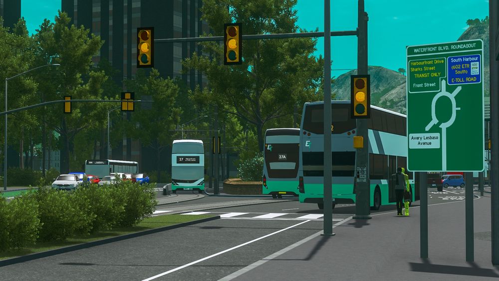 Pedestrian-height view of one end of a signalized roundabout. Buses and cars drive through, and there is a navigational sign for the roundabout on the left-hand side of the image.