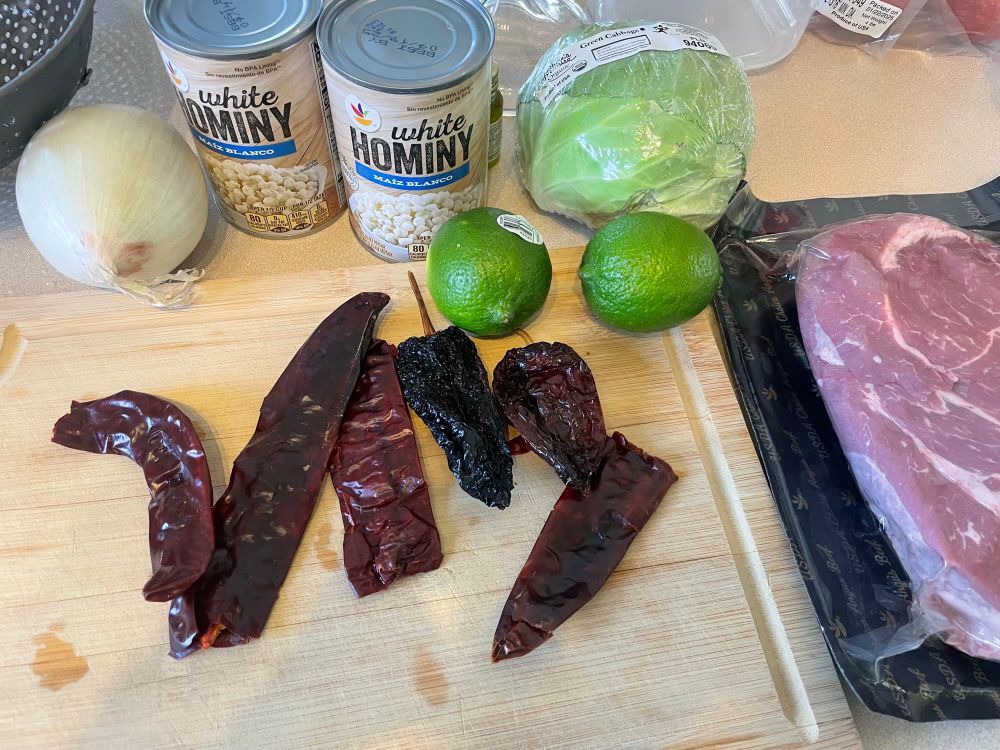 Pictured: ingredients for pozole.  Dried chilis, limes, onion, hominy, cabbage, and pork.