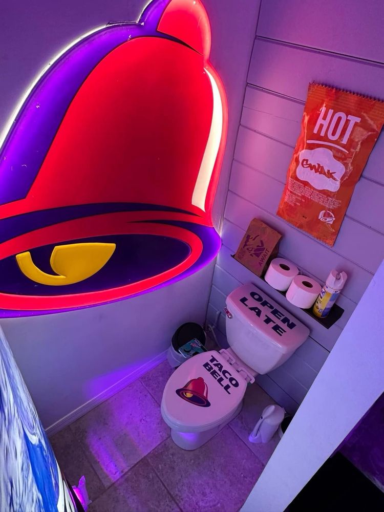A Taco Bell bathroom with a giant bell light 

A giant hot sauce pack art
The toilet says Taco Bell on it open late

There’s a Baja blast bidet attachment
