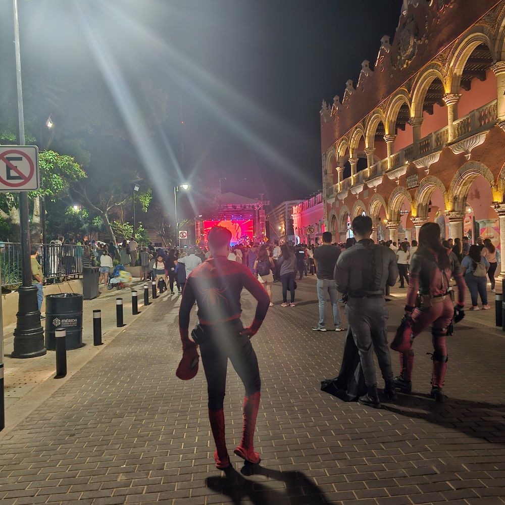 Unmasked Spiderman, Batman, and Deadpool watching outdoor Merida concert featuring Maria Leon