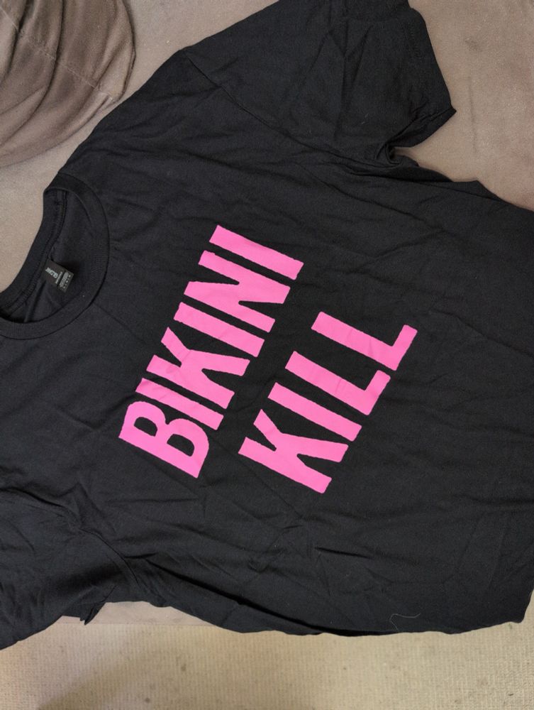 A black T-shirt with a dark rose-pink colored block text of the band name Bikini Kill, so it reads as BIKINI KILL 