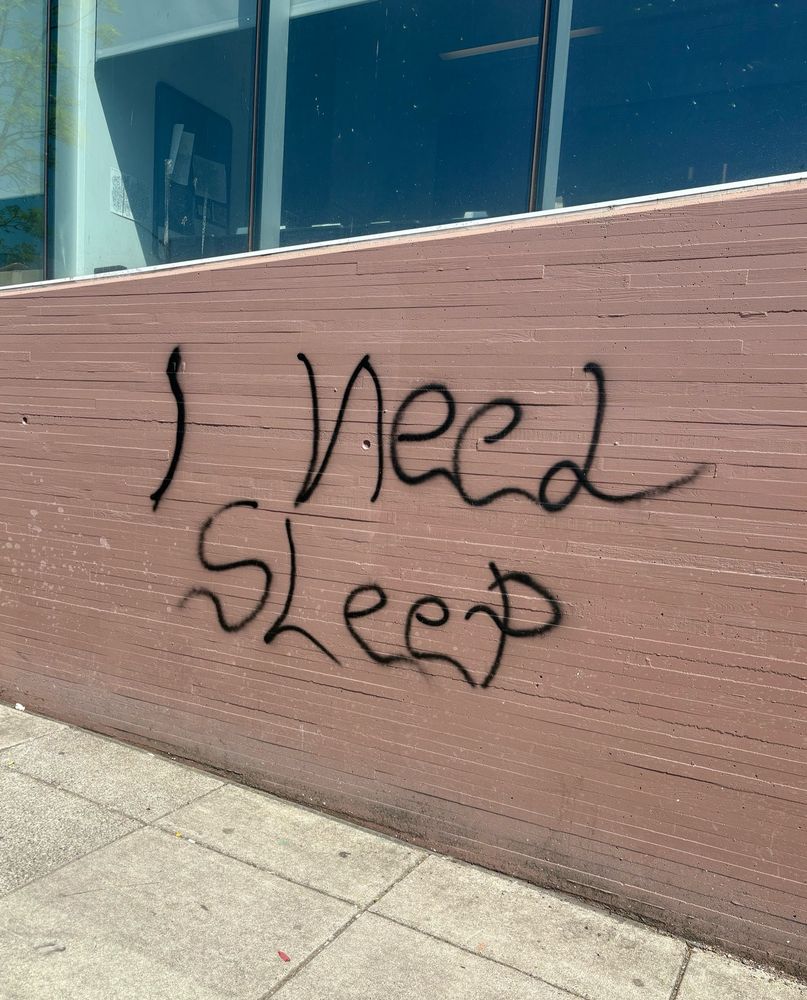 original image of a building on Broadway in. NW Portland with teal windows with “I need sleep” scrolled on the terracotta colored wall in graffiti 
