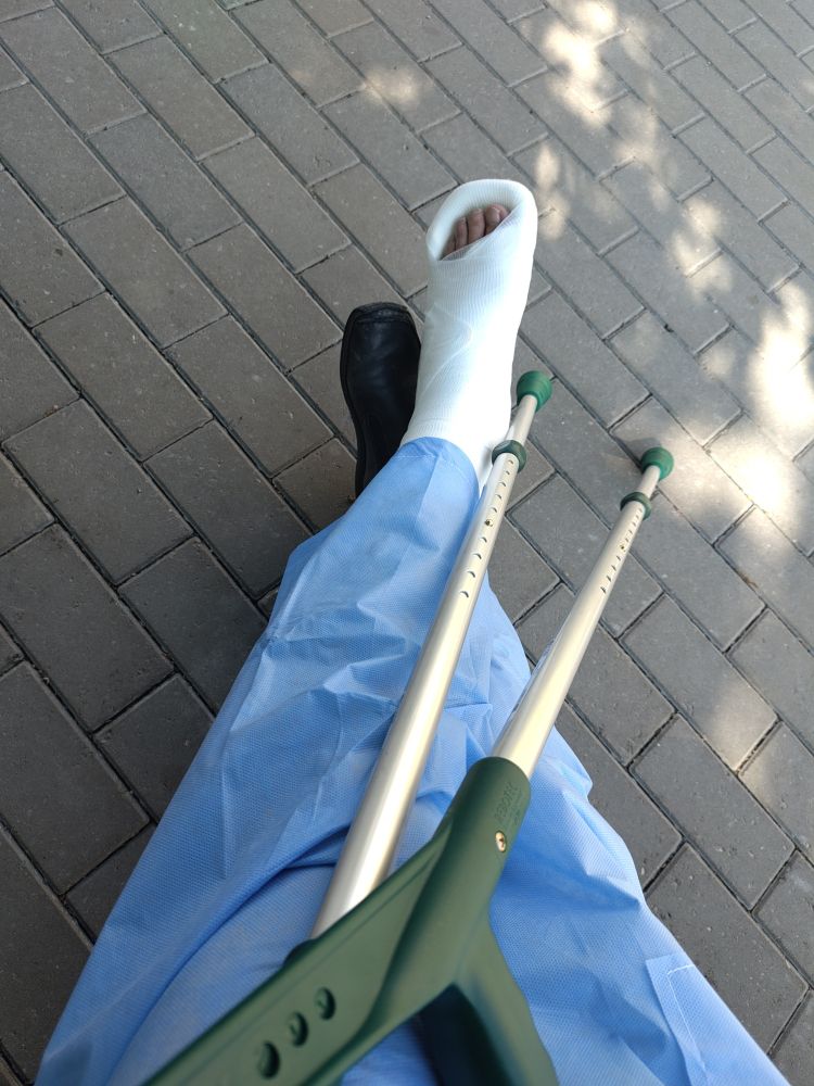 Feet in blue hospital pants and crutches. One footcis in a cast.
