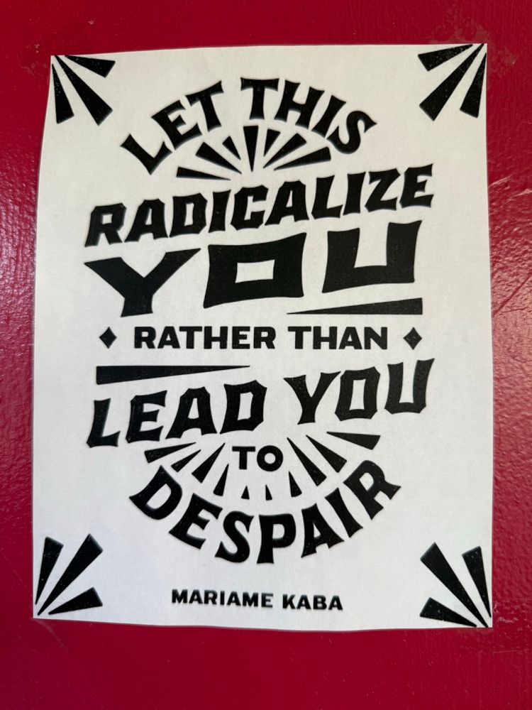 A poster reading: “Let this radicalize you rather than lead you to despair.” On a red wall.