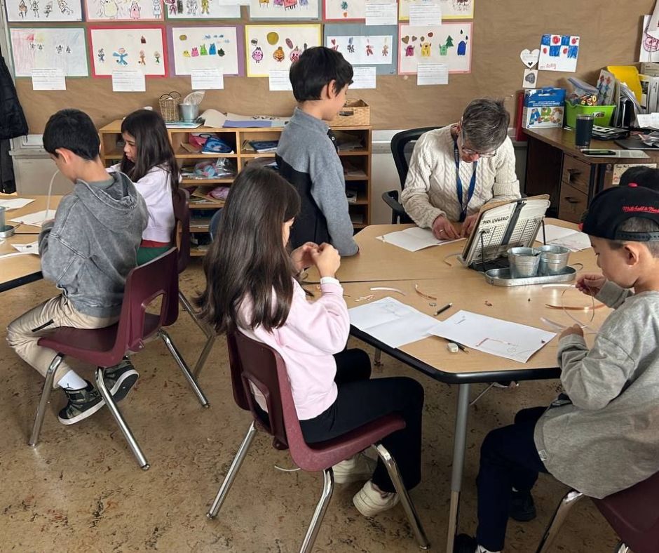 A group of young students in a classroom, engaged in a STEM activity. The room is decorated with various artworks and educational materials.