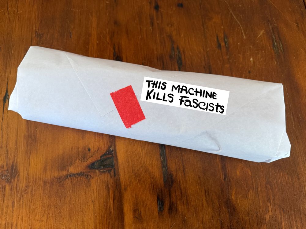 Same wrapped sub sandwich, with a "THIS MACHINE KILLS FASCISTS" sticker edited in. 