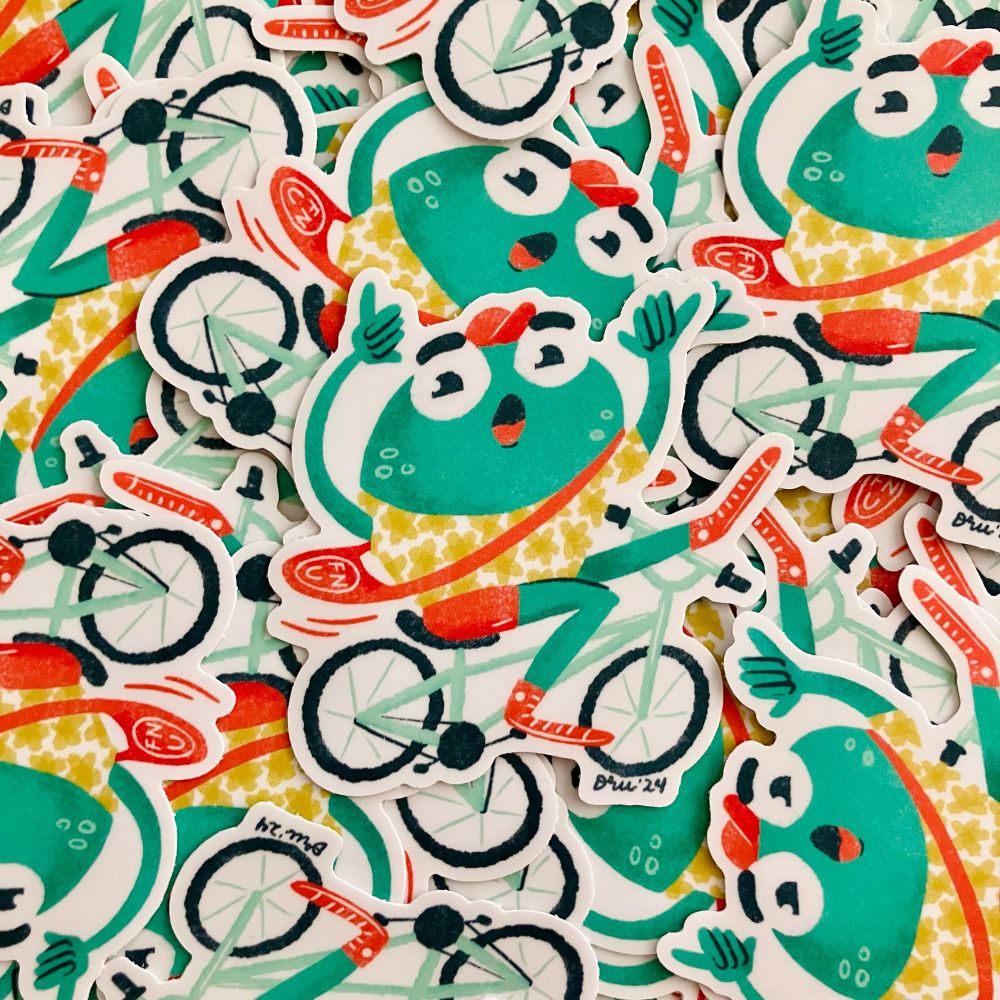 Photo of a pile of stickers. The sticker design is an illustration of a green frog in an aloha shirt riding a bicycle and throwing up shakas with both hands.