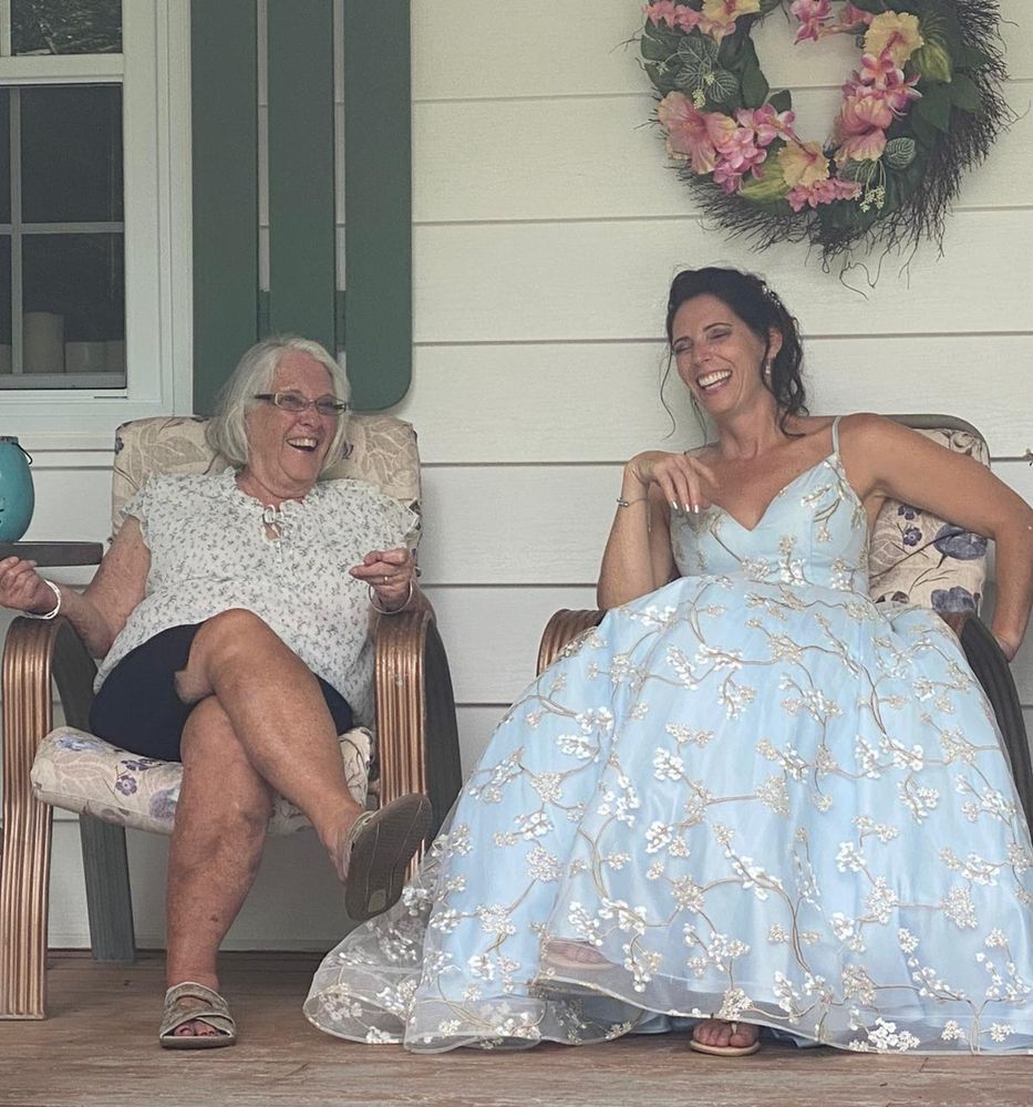 A beautiful woman sits on the veranda with her daughter. Both are smiling and laughing, happy to be together on the day of the daughter's wedding. 