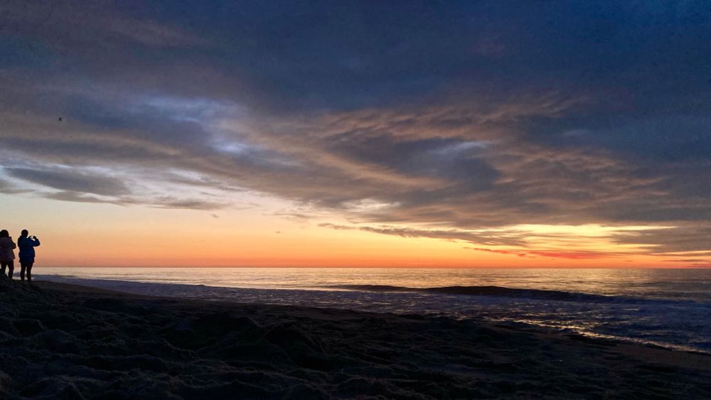 A silhouette of two females standing before the ocean, taking what appears to be a photo or video of the sky before sunrise. 
Taken this morning at 5:47 a.m..